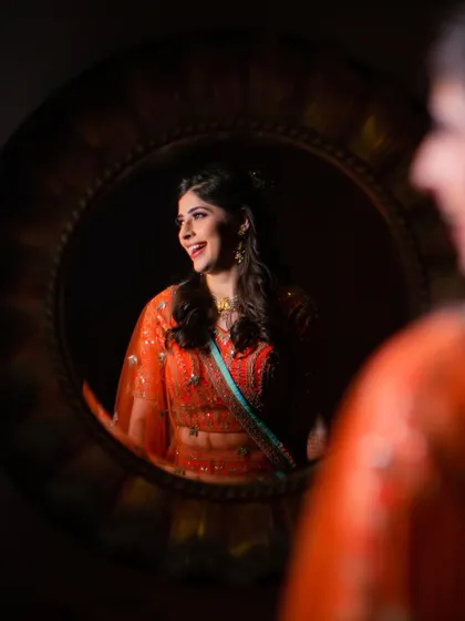 A creative shot of the bride's reflection in a mirror. Her joyful, candid laugh is captured, showing a moment of pure happiness while getting ready.