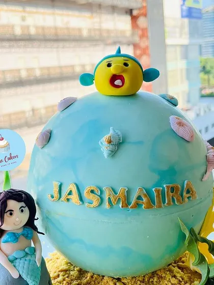 A close-up of a unique mermaid-themed piñata cake, designed as a large sphere with a mermaid and fish character on top.