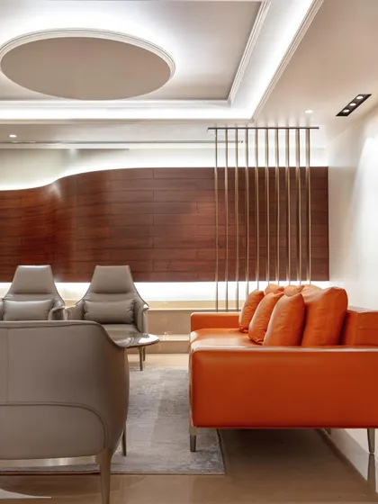 In the formal living room of the Wanderlust Villa, a bold orange sofa provides a vibrant contrast to the neutral tones and curved wood-paneled wall. The design is a balance of modern energy and timeless sophistication.