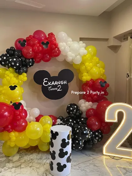 A classic Mickey Mouse theme for a second birthday. This decoration features a circular balloon garland in Mickey's iconic red, yellow, black, and white, with a custom cutout sign and a light-up number '2'.
