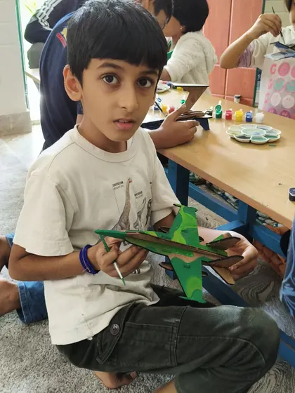 A young creator puts the finishing touches on his camouflage-themed fighter jet. This activity helps develop fine motor skills and attention to detail.