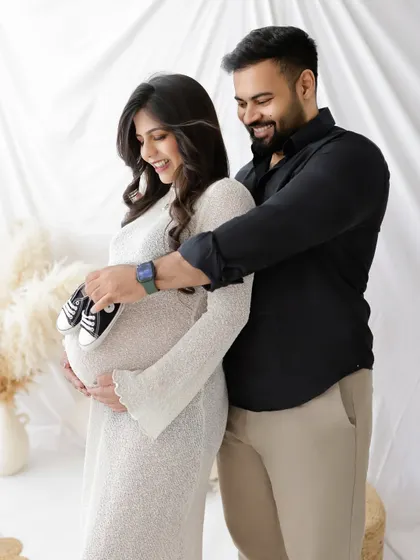 A playful and sweet photo of a couple with tiny baby shoes. The dad-to-be holds the shoes up to the baby bump, a cute way to show they're ready for their new arrival.