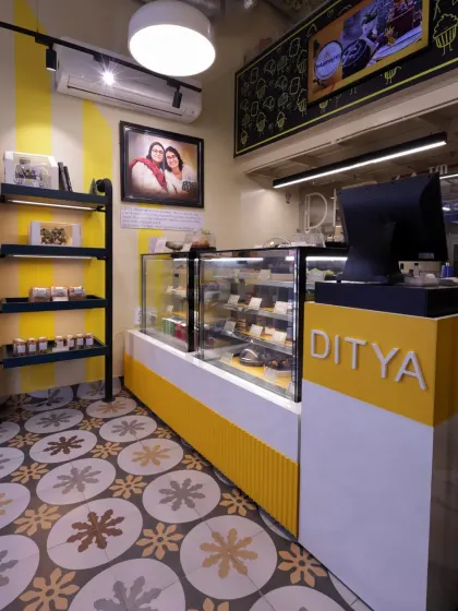 The main service counter at Ditya Bakehouse, designed with a cheerful yellow base and clean white top. The vibrant Moroccan-style floor tiles and chalkboard menu add a playful, artisanal charm to this bakery.