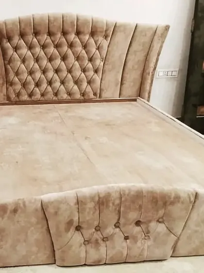 The frame of a custom-made bed during production. This piece features a tall, curved headboard with classic diamond-tufted cushioning.