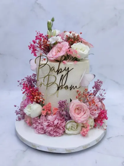 A beautiful "Baby in Bloom" cake, perfect for a baby shower or first birthday. This two-tiered cake is lavishly decorated with a cascade of fresh pink and white flowers and delicate wafer paper butterflies.