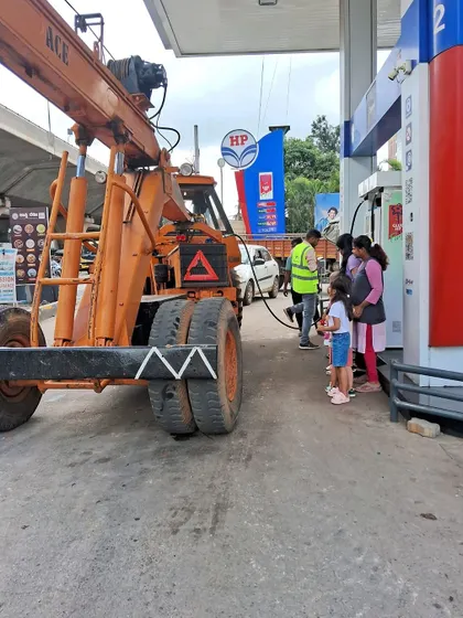 The children observe a large crane at the petrol pump, sparking their curiosity about different types of vehicles.