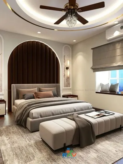 A grand master bedroom with a dark wood arched headboard, creating a dramatic focal point. The room features a cozy window seat, a crystal-accented fan, and a luxurious, plush feel.