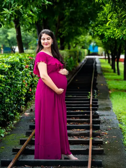 A beautiful solo portrait of the mom-to-be in a magenta gown, standing on a rustic railway track, symbolizing the journey ahead.