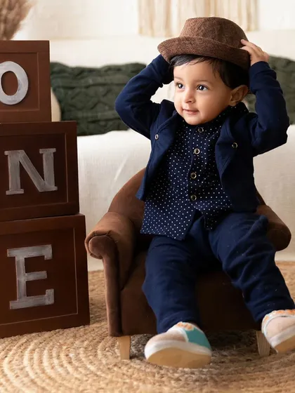 This little gentleman is adjusting his hat in a playful pose next to 'ONE' blocks during his first birthday portrait session.