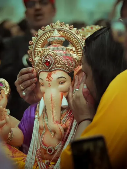 An intimate, close up moment where a devotee gently touches a small Ganesh idol's face in a final farewell.
