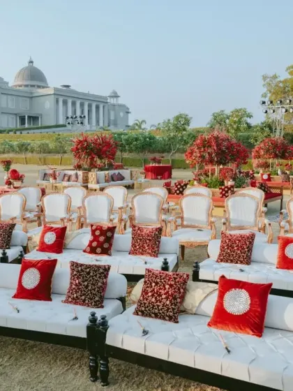The guest seating arrangement combines traditional low diwans with elegant chairs, all facing the majestic palace. The rich red and patterned cushions tie into the 'Gulal Bagh' theme perfectly.
