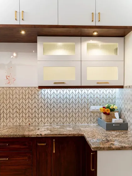 The finished kitchen corner, with beautiful glass tiles, a granite countertop, and a mix of wood and white cabinets. Under-cabinet lighting highlights the workspace and the decorative backsplash.