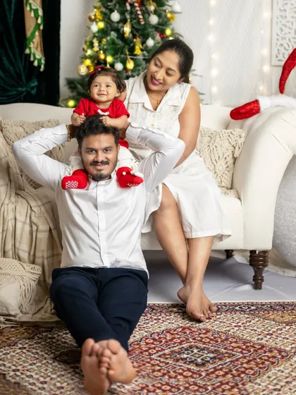 A playful moment between parents and their little one, who is sitting on her father's shoulders.
