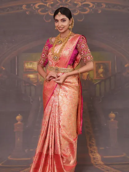 A model in a pink silk saree, styled with a traditional gold-finish long haram and matching vaddanam.