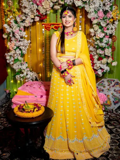The bride posing next to a traditional 'thali' at her Haldi ceremony. The decor includes a floral arch and colorful elements that enhance the festive mood.