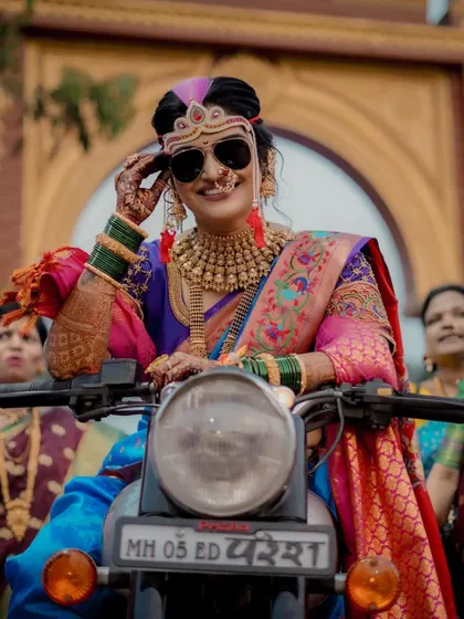 The epitome of a cool bride. She sits confidently on a motorcycle, wearing sunglasses with her traditional Maharashtrian wedding attire.