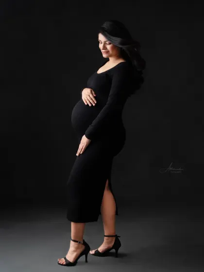 A graceful profile shot. This pose is perfect for highlighting the beautiful curve of the baby bump in a sleek, black bodycon dress.
