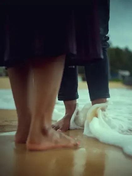 A low-angle shot of a couple's feet in the sand as the waves wash over them, capturing a small, sensory detail of a beach pre-wedding shoot.