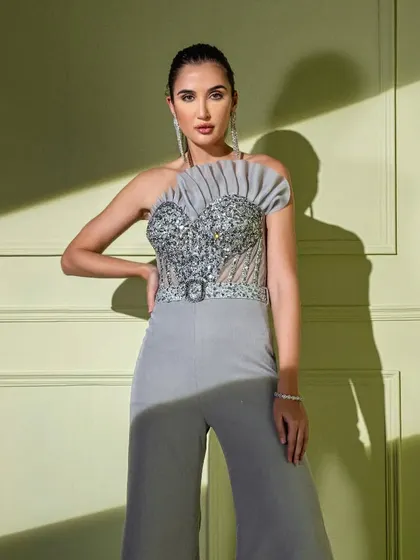 A statement in grey, this jumpsuit features a fully embellished corset top with a unique pleated fan detail on one shoulder. The belted waist and wide-leg trousers create a chic, contemporary silhouette.