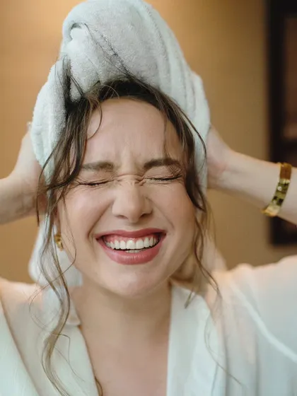 A candid moment of pure joy from a cinematic portrait session. The model's spontaneous laughter while drying her hair creates an authentic and relatable image.