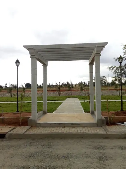 A simple, modern concrete pergola structure installed at the entrance of a path in a developing landscape. This acts as a gateway and a frame for the view beyond.