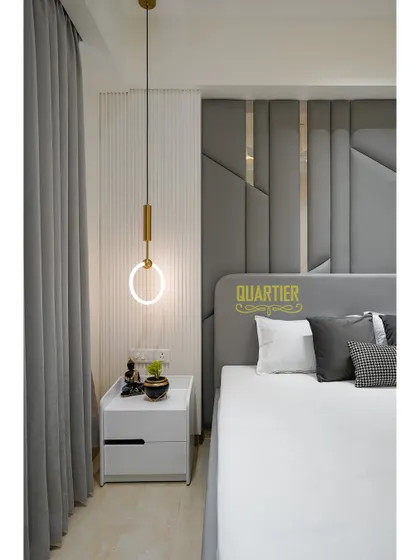 A detail of the bedside in the Tata LaVida guest room. The combination of the grey quilted headboard, the vertical fluted panel, and the modern ring-shaped pendant light creates a chic and contemporary look.