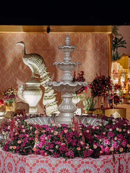 A beautiful fountain centerpiece surrounded by a bed of pink and purple flowers, with a peacock statue adding a touch of regal Indian symbolism.