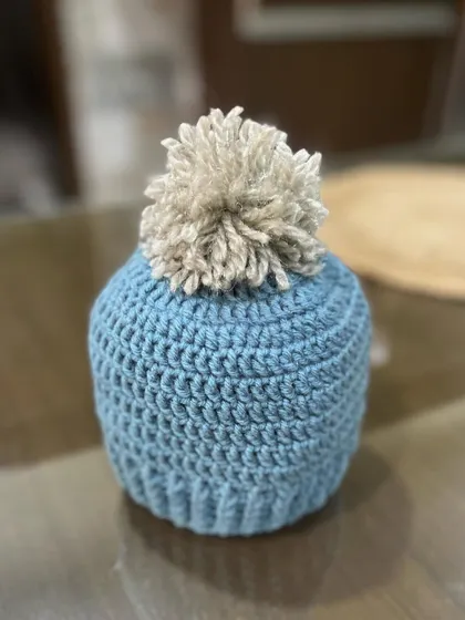 Another look at the blue baby beanie with a beige pom-pom. This classic color combination makes it a lovely and timeless gift for any newborn.