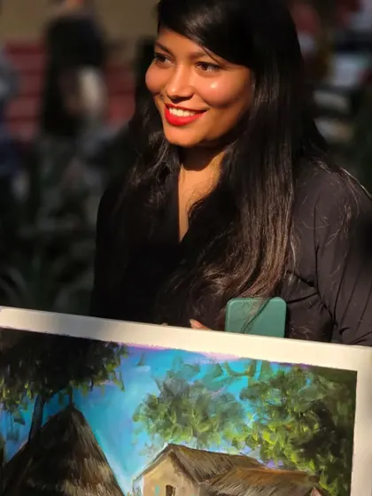 A student proudly holds up her finished landscape painting from our outdoor session, her smile reflecting a day well spent creating art in nature.