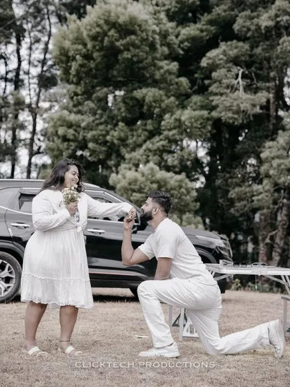 A sweet proposal moment in a field in Ooty, with the groom on one knee in front of their car.