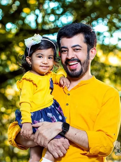 A father holds his young daughter, both smiling brightly in matching yellow outfits. This outdoor portrait is full of warmth, happiness, and vibrant color.