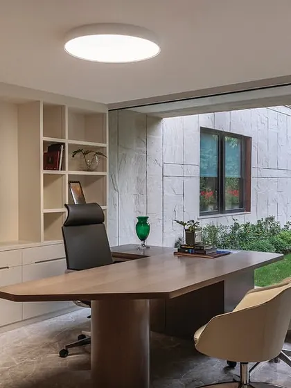 A director's cabin in 'The Layered Office' designed with clean lines and a neutral color palette. A large window provides a view of the outdoor garden, bringing a sense of tranquility to the executive workspace.