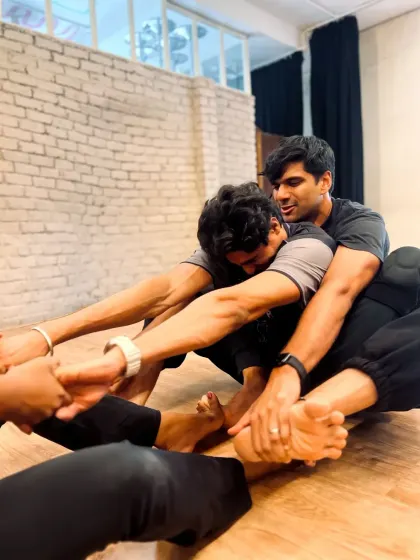 A group of students works together on a seated forward fold, using teamwork to help each other achieve a deeper stretch.