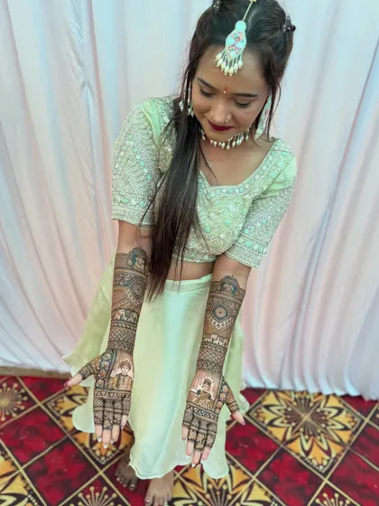 A beautiful bride in her green lehenga, perfectly complementing her intricate bridal mehndi. Her hands tell a story with detailed portraits and traditional designs.