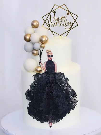 A sophisticated cake for the diva on her special day. This two-tiered white cake features an elegant edible print of a woman in a stunning black lace gown, accented with a balloon-like cluster of white and gold spheres.