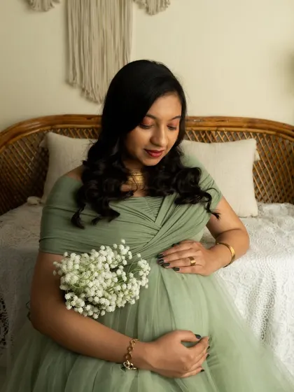 A close-up portrait in a sage green gown, holding a bouquet of baby's breath. The focus is on the mother's gentle expression.