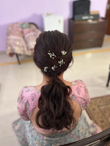 A messy ponytail with a textured crown and delicate baby's breath flowers tucked in. This is a romantic and soft look, perfect for an engagement.