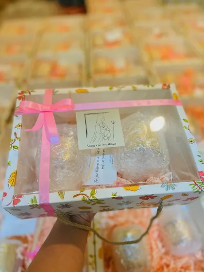 A single wedding favor box held up to show the clear lid, revealing the two elegant mercury glass candles inside.
