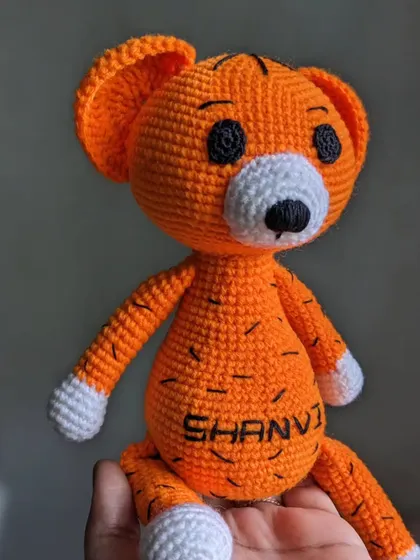 A bright orange tiger plushie, personalized with the name 'SHANVI' on its tummy. The black stripes are all hand-stitched.