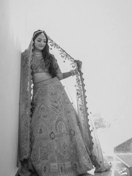 A graceful black and white portrait of the bride leaning against a wall, her veil flowing. The simplicity of the shot highlights her elegance.