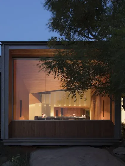 A view through the trees reveals the carefully orchestrated interior lighting. The goal was to create a visual beacon that feels both modern and deeply tied to its natural surroundings.