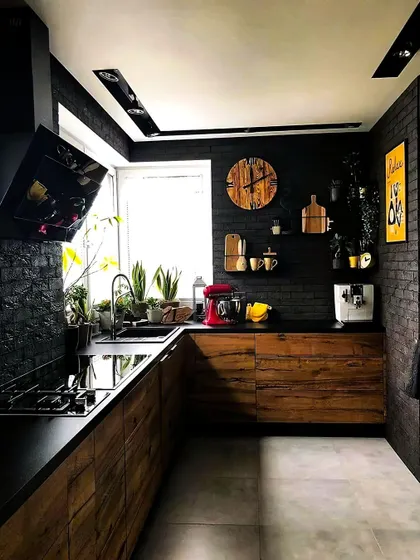 For a bold and moody atmosphere, this kitchen pairs dark wood cabinets with a textured black brick wall. The design is rustic yet modern, with open shelving and countertop plants adding life and personality to the space.