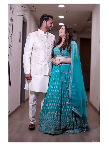 A full-length portrait of the engaged couple in a well-lit corridor, showcasing their coordinated white and turquoise outfits.