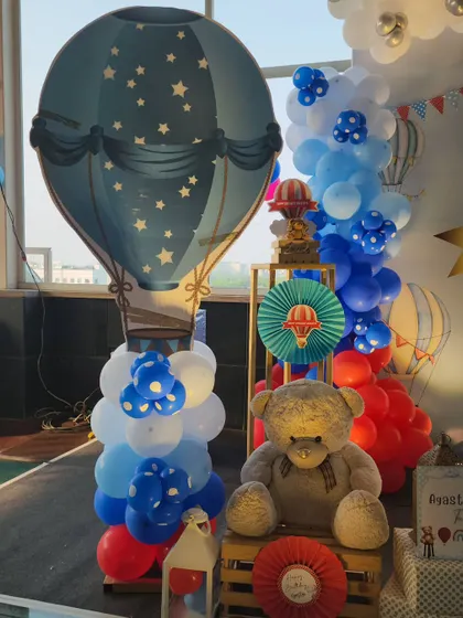 A detailed shot of the decor next to the main stage. It features a large teddy bear, a blue hot air balloon cutout, and a column of blue and white balloons, creating a full and festive look.
