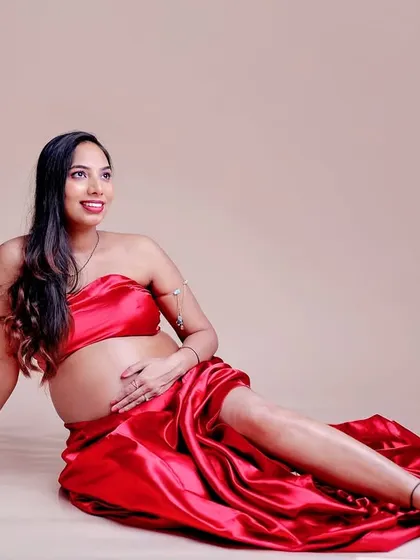 A relaxed and confident pose in a red satin fabric wrap. This style is perfect for highlighting the baby bump in a bold and beautiful way.