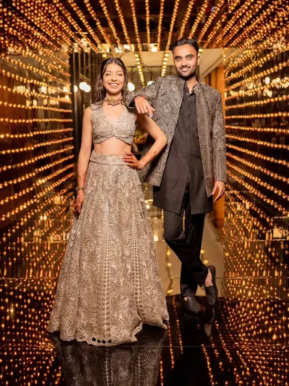 The couple poses in a tunnel of golden fairy lights, a perfect photo-op that combines glamour and romance, fitting the dazzling vibe of their Sangeet night.