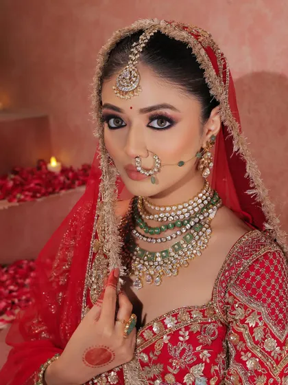 The bride looking directly at the camera, her gaze intensified by the kohl-rimmed eyes and dramatic liner. The red dupatta frames her face, completing the traditional bridal picture.