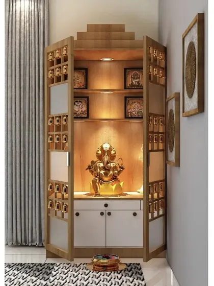 A unique corner pooja unit design with doors that feature small bells and glass panels. The interior is lit to highlight a golden Ganesha idol, creating a peaceful and auspicious corner.