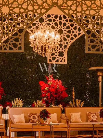 Another view of the lounge area under the jaali arches. The space is filled with plush seating and accented with deep red florals, creating a perfect blend of modern design and royal elegance.