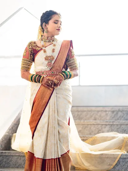 A full-length view of this classic Muhurtham look. The elegance of the white and maroon Kanjivaram saree is complemented by the intricate blouse embroidery and traditional temple jewelry.